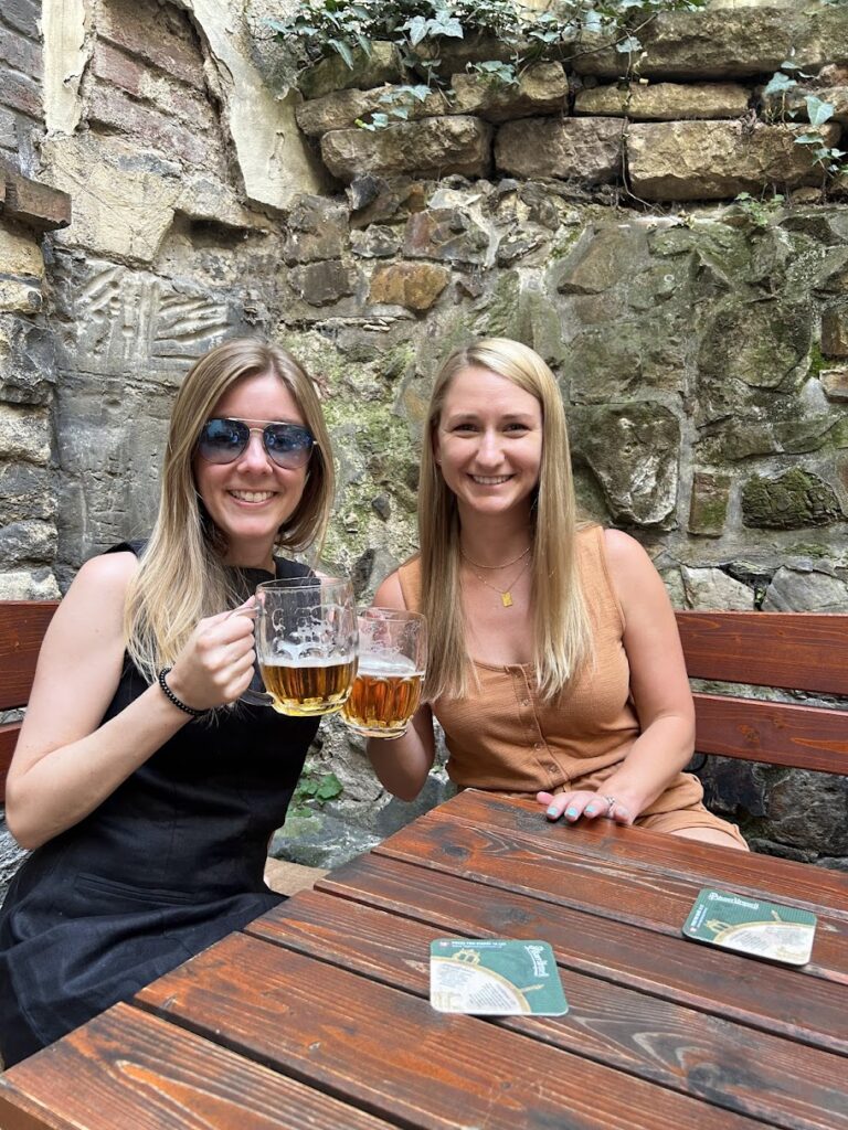Two women sitting at a table holding beers in Prague.