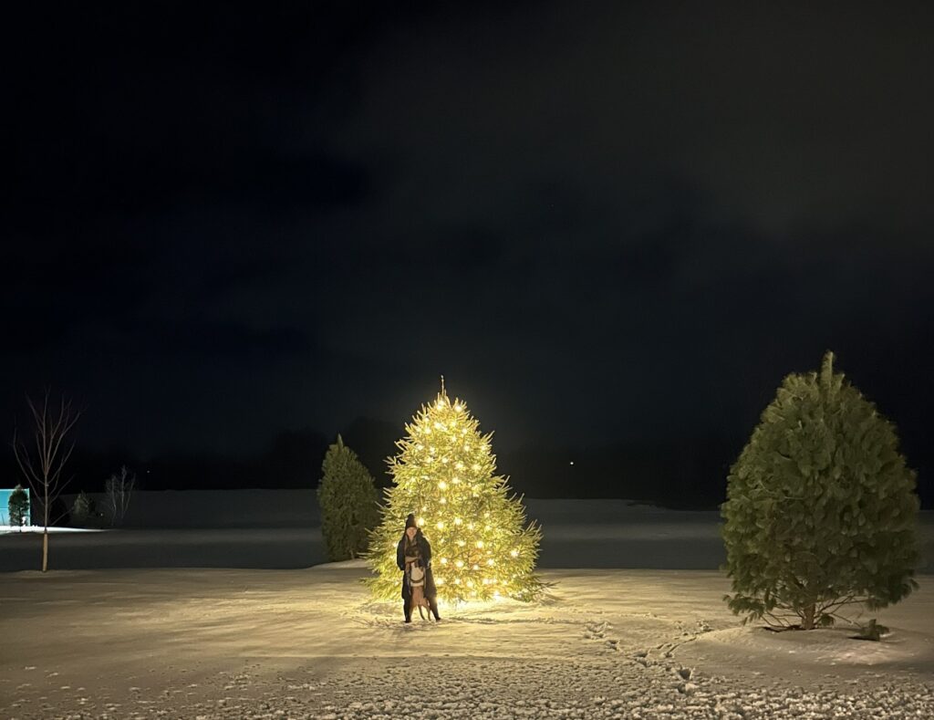 A guest and her pet dog in front of a lit-up Christmas tree at Skaneateles Fields Resort & Spa