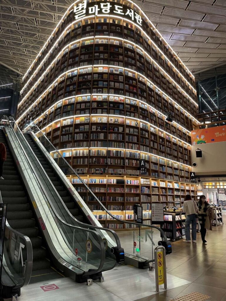 Interior view of Starfield Library at COEX Mall in Seoul with towering 13-meter bookshelves and visitors browsing and taking photos.”
