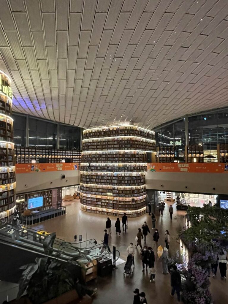 Wide shot of the open library atrium showing curved wooden shelves filled with books and reading tables beneath soft ambient lighting.
