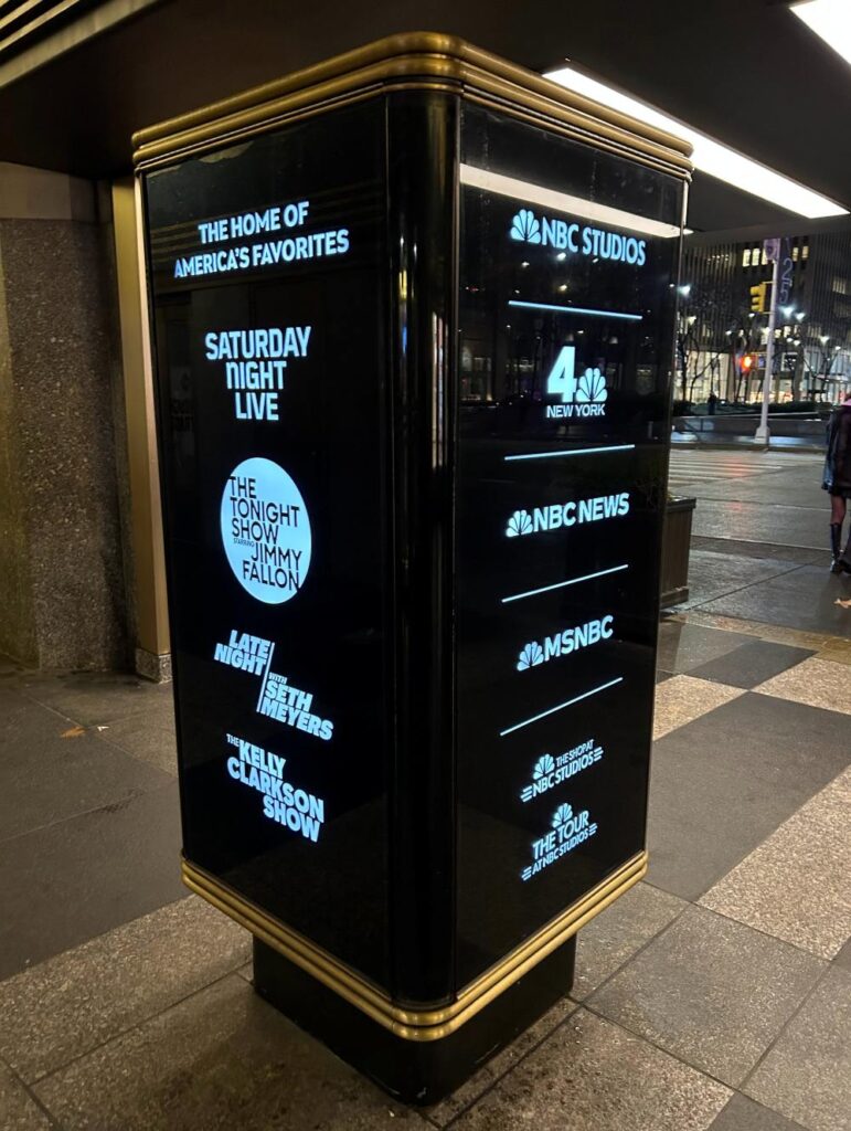 Outside 30 Rockefeller Plaza, New York, a display of studio names and popular shows like Saturday Night Live.