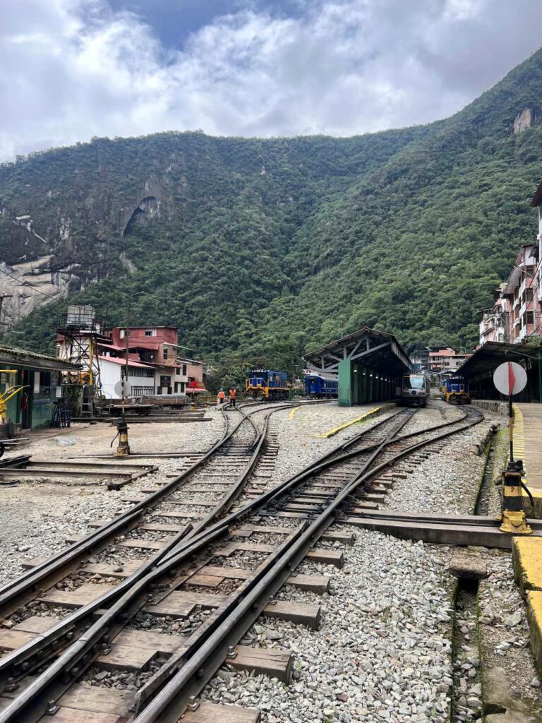 Exterior view of Aguas Calientes railway station with trains arriving amid lush mountain scenery near Machu Picchu