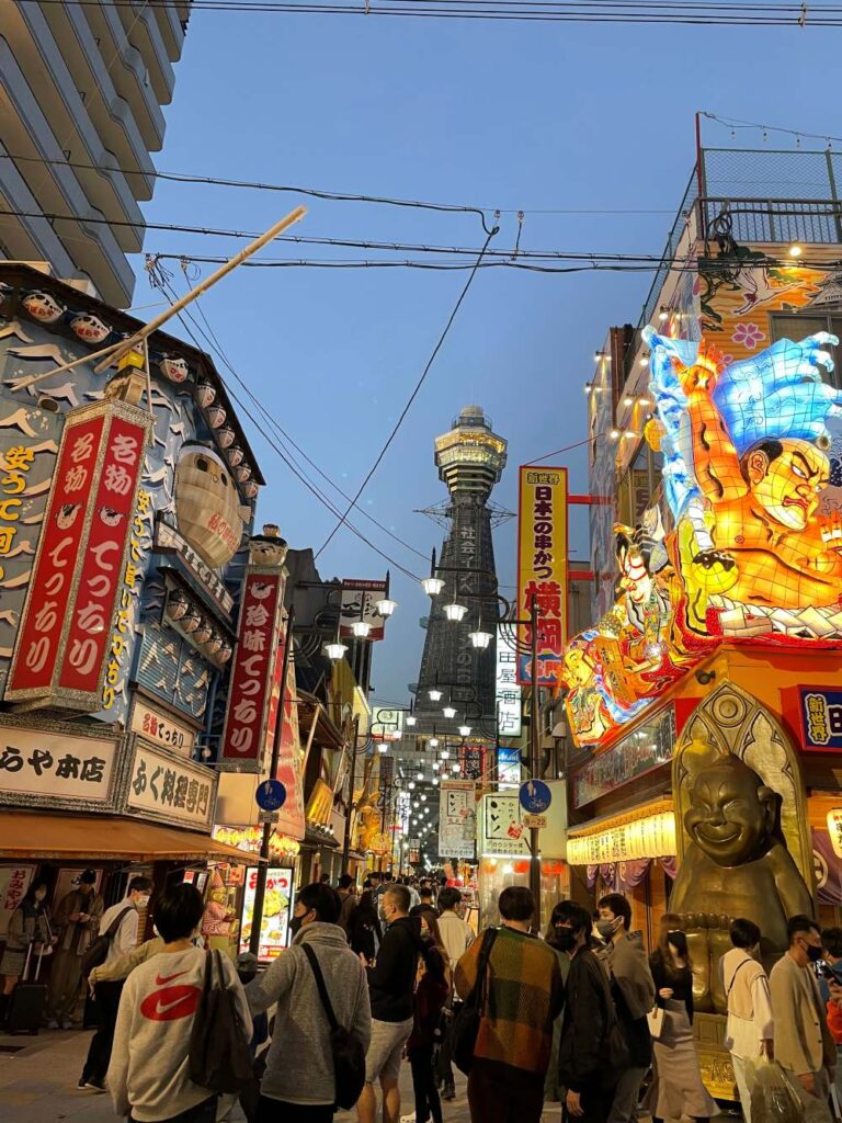 Shinsekai at night with illuminated restaurant signs, lively streets, and Tsutenkaku Tower in the background