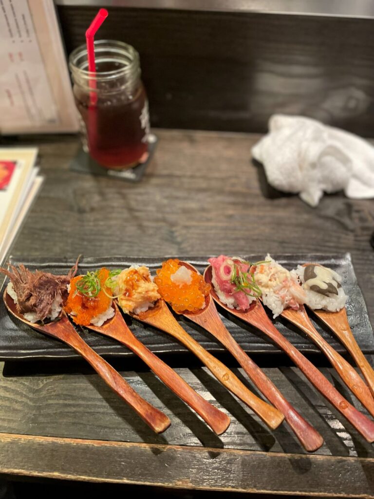 a 7-piece assortment of signature spoon sushi served on wooden spoons, highly characteristic of the popular menu item at SUSHI & GRILL SOUYA in Namba, Osaka